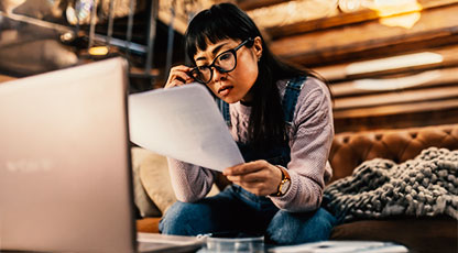 Image of a women reading a document and looking at a laptop
