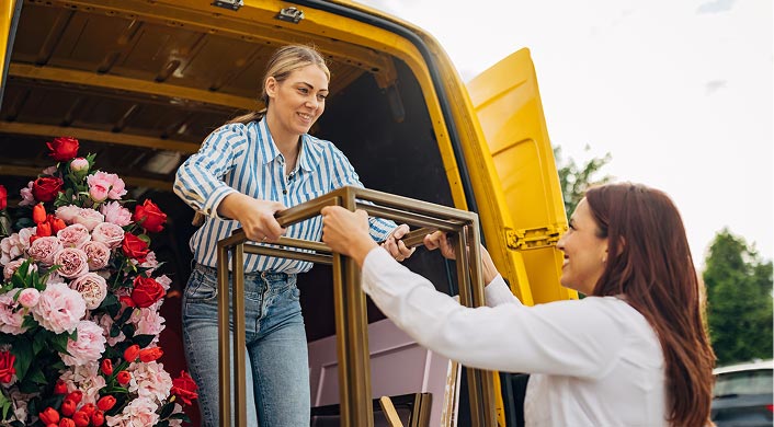 Person handing a side table to another person out of the back of a flower shop buss