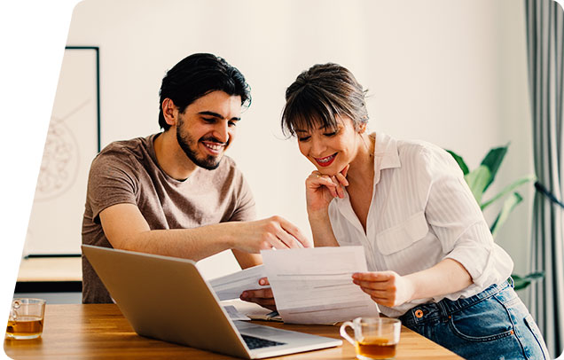 Image of two young people at a dining table looking at monthly bills and a computer