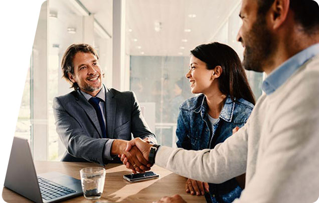 A loan advisor shakes hands with a young couple in an office setting