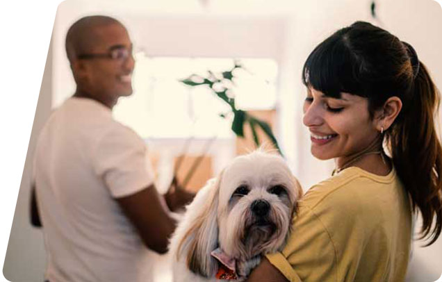 A person smiles while holding a dog as their partner looks on and smiles