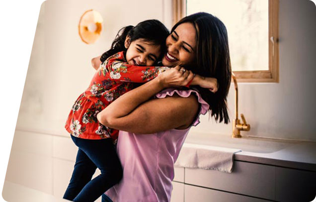 A smiling parent holds up their young child who is laughing
