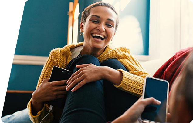 A young adult laughs with the person across from her as both people hold onto their phones