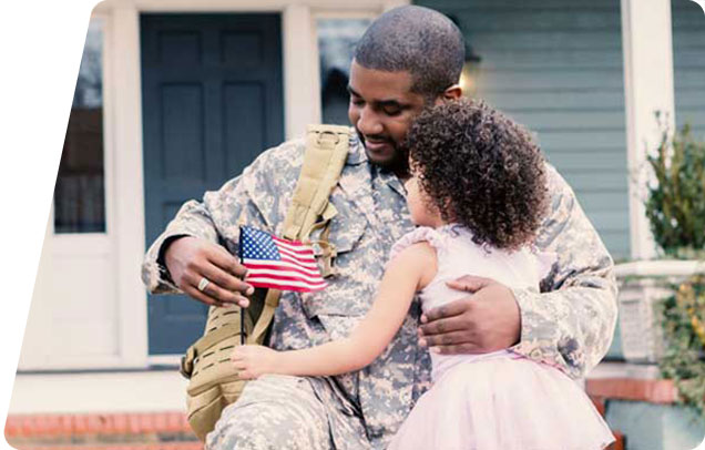 A child with a miniature American flag in hand hugs her parent dressed in military fatigues