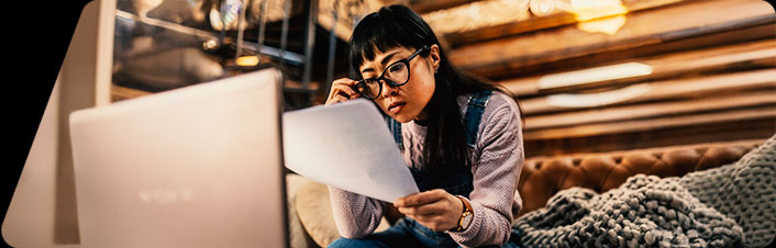 Image of a women reading a document and looking at a laptop
