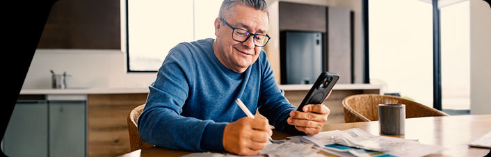 Man reviewing documents and using his smartphone at home to manage finances.