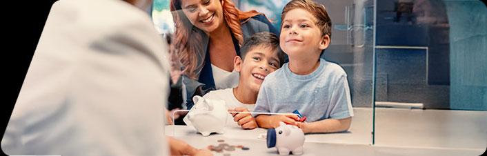 Image of a woman and two children with piggy banks at a bank counter exchanging coins with a banker